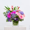 Pink orchids and roses with purple hydrangeas in a clear glass vase