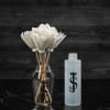 White artificial flowers in a clear glass vase beside a frosted bottle