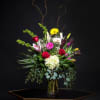 Tall mixed bouquet in a glass vase with roses, lilies, and bright accent flowers