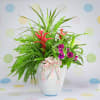 Tropical floral arrangement in a white vase with pink ribbon
