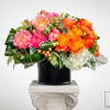 Bright pink peonies, orange roses, and white hydrangeas in a black cylinder vase