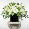 White floral arrangement in a black vase with trailing greenery