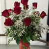 Red roses arranged with white baby's breath in a clear glass vase.