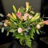 Pink lilies and peonies arranged in a glass vase with greenery.