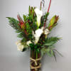 Tall arrangement of white calla lilies and red tropical blooms in a glass vase