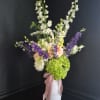 Tall purple delphinium spires rise above a lush base of green hydrangeas