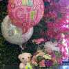 Pink baby girl balloon with flowers, teddy bear, and floral arrangement