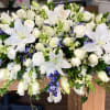 Large white floral casket spray with lilies, roses, and blue accents