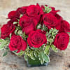 Red roses arranged in a clear glass vase with variegated greenery
