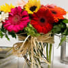 Bright gerbera daisies arranged in a clear square vase with raffia ribbon