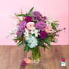 Mixed pink, purple, and white flower arrangement with hydrangea in a clear glass vase
