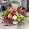 Mixed bouquet of roses, orchids, and purple flowers in a white vase
