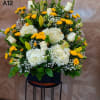 Large floral arrangement with white roses, hydrangeas, and yellow daisies in a black container