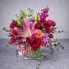 Pink lilies and red roses arranged in a clear glass vase with ribbon.