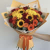Hand-tied bouquet of yellow sunflowers, red roses, and orange blooms in orange wrap with ribbon