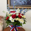 This patriotic arrangement features blooms such as delphinium, roses, and carnations. Perfect