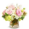 Low arrangement of pink roses and mixed pastel flowers in a clear glass vase with curly branches.