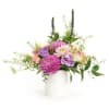 Mixed arrangement of pink and purple flowers with peach accents in a white cylinder vase