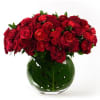 Low round arrangement of red roses and ranunculus in a clear glass vase lined with a large green leaf.