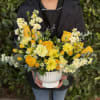 Yellow and cream flower arrangement with roses and daisies in a white ribbed ceramic pot