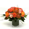 Low orange and peach rose arrangement with pincushion protea in a glass cylinder vase.