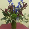 Tall vase arrangement with blue flowers, burgundy roses, and a green moss ball