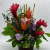 Tropical flower arrangement in a dark container with red and orange blooms