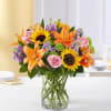 Bouquet of sunflowers, orange lilies, and pink roses in a glass vase