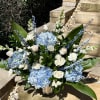 Blue hydrangeas and white roses arranged in a vase with tall blue accents