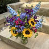 Bouquet of sunflowers, blue delphinium, purple blooms, and pink roses in a glass vase
