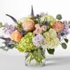 Bouquet of peach roses, hydrangeas, and purple flowers in a glass vase
