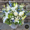 White lilies and roses with blue accents arranged in a clear patterned glass vase