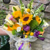 Bright mixed bouquet with sunflowers, lilies, snapdragons and purple blooms wrapped in mesh with ribbons.
