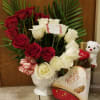 Red and white roses in a white vase with chocolates and a teddy bear