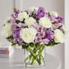 White roses and purple flowers arranged in a clear glass vase