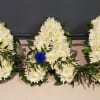 Three floral letters made of white flowers with blue roses and greenery accents.