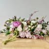 Low centerpiece of pink hydrangeas, white roses, and a bright pink peony on a wooden table