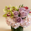 Low arrangement of lavender roses, green orchids, and blush hydrangeas in a glass vase