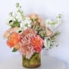 Soft pink chrysanthemums and coral-peach roses spill from a warm ribbed amber