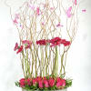 Pink roses and gerbera daisies in a gray bowl with tall curly branches and butterflies