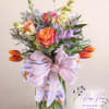 Mixed bouquet in a glass vase with orange roses and tulips, tied with a patterned ribbon.