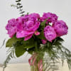Pink peonies arranged in a clear glass vase with trailing greenery