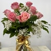 Pink roses in a glass vase with white baby's breath and a gold ribbon