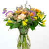 Mixed bouquet of yellow, purple, and peach flowers in a clear glass vase