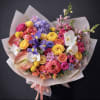 Colorful mixed bouquet with roses, orchids, and irises wrapped in pale paper