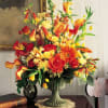 Tall arrangement of orange, yellow, and red flowers in a green pedestal vase