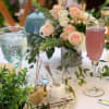 Pastel rose centerpiece with greenery on a table beside drinks and jars