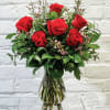 Red roses arranged in a clear glass vase with small pink filler flowers.