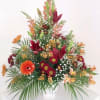 Tall mixed floral arrangement in a white vase with orange and burgundy blooms