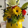 A glossy yellow ceramic smiley-face vase holds a cheerful mixed bouquet that